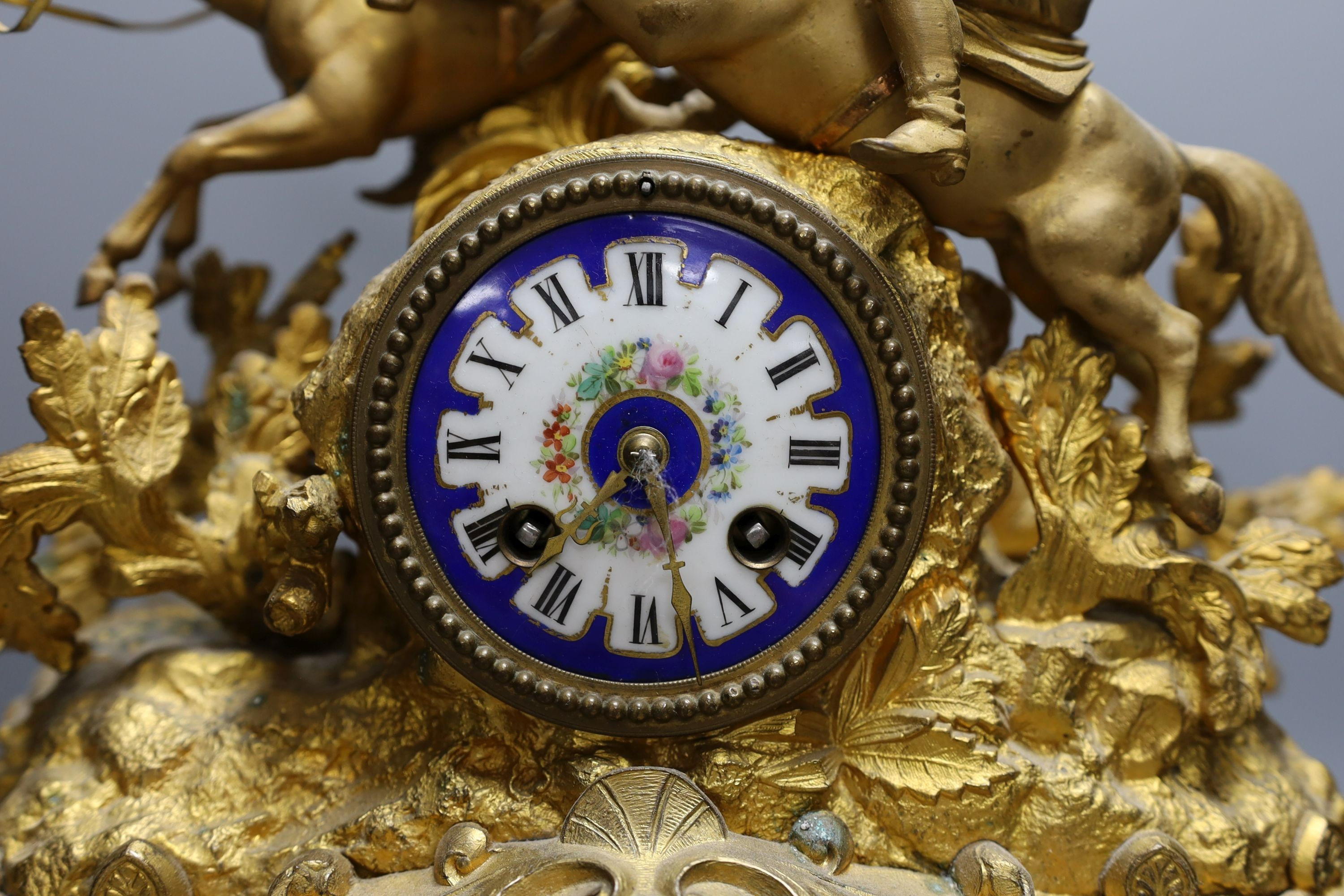 A 19th century gilt spelter mantel clock, having horse and jockey surmount with porcelain panels and circular porcelain dial, on shaped plinth base. 47cm